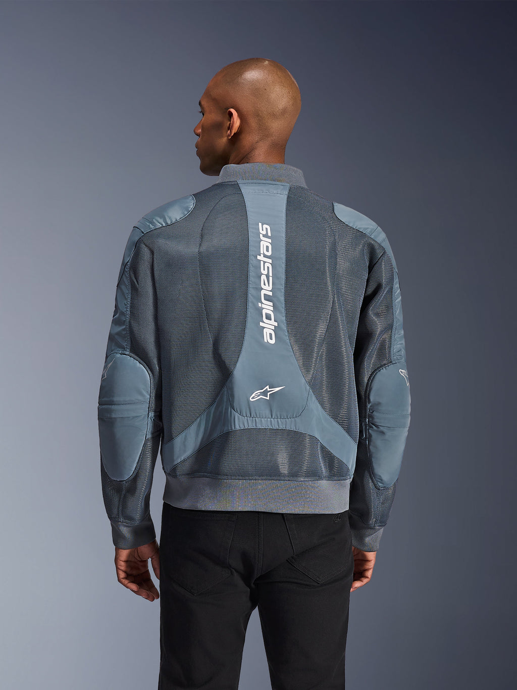 Alpinestars Flight Air-jacka i Storm Gray, baksida på en modell, urban motorcykeljacka med utökade 3D-meshpaneler, vertikal Alpinestars-märkning på ryggen samt ribbad fåll och krage i bomberstil.