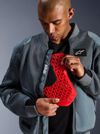 Alpinestars Flight Air-jacka i Storm Gray, urban mc-bomberjacka med 3D-meshpaneler för luftflöde, öppen för att visa ett rött Nucleon-ryggskyddsinlägg, med 'Alpinestars Protects'-branding och en modern streetwear-estetik