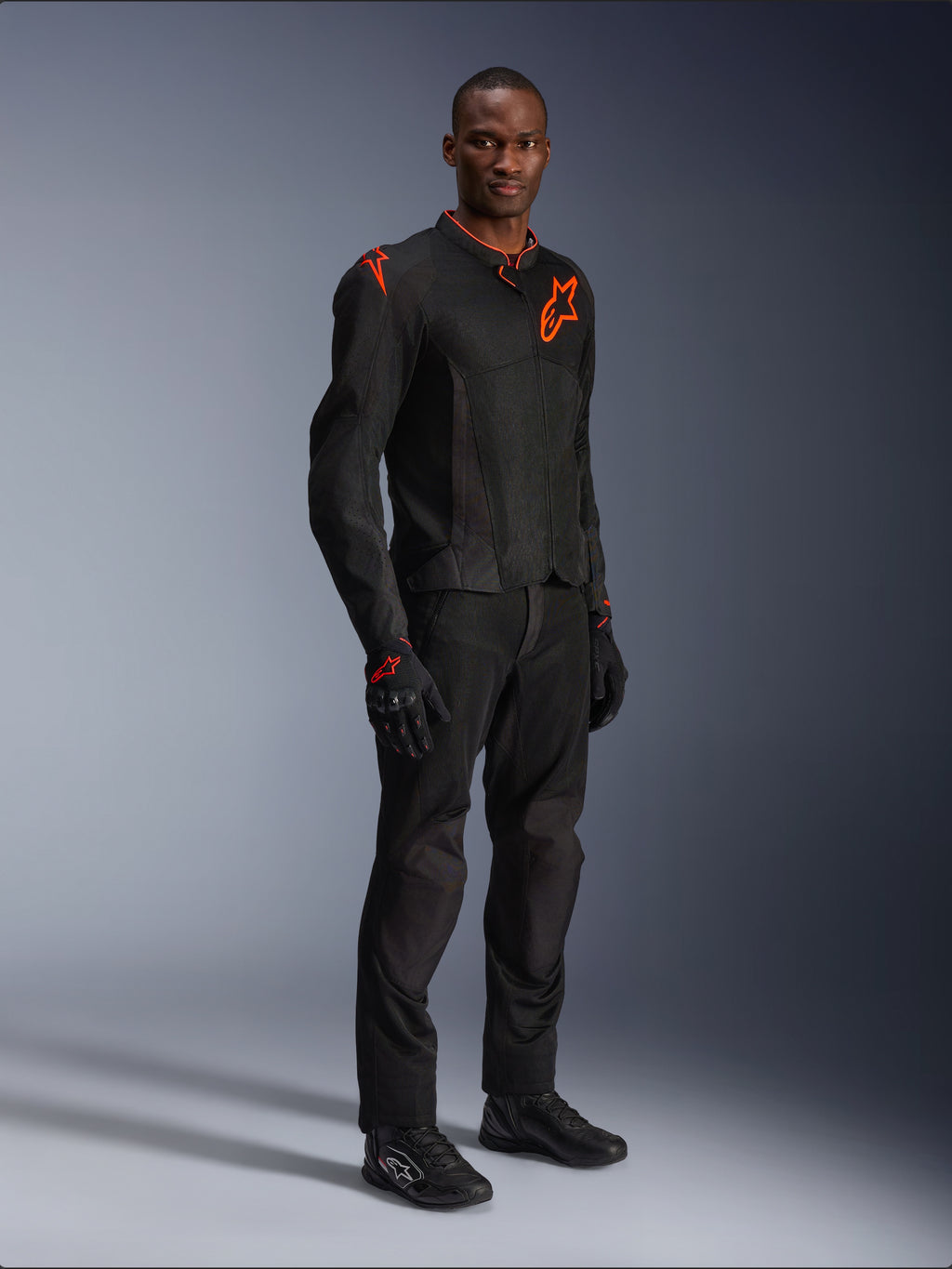 Model wearing Alpinestars Viper Air V4 Jacket in Black and Red Fluo, featuring mesh panels and red star logos on the chest and shoulder, paired with matching black motorcycle pants, gloves, and riding shoes, professional road riding gear ensemble