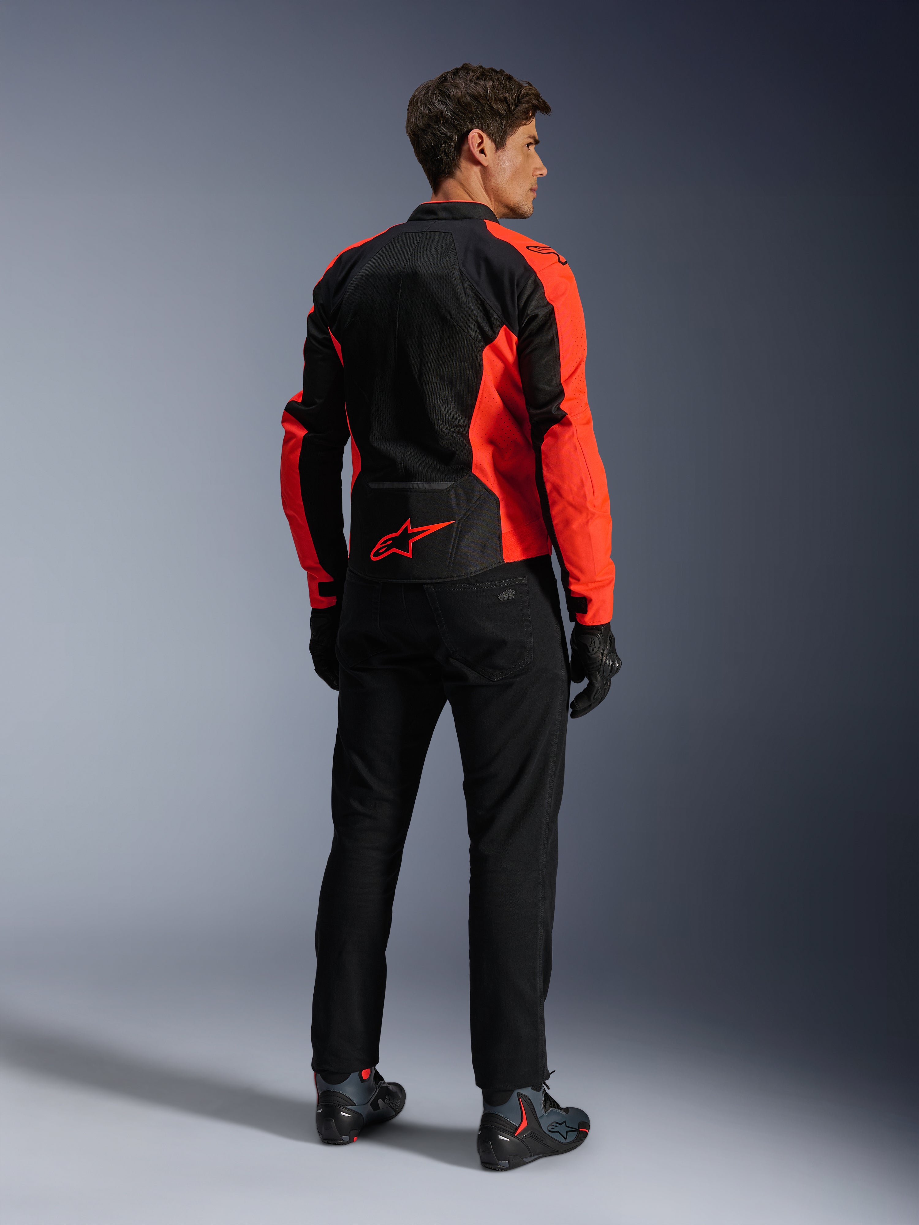Alpinestars Viper Air V4-jacka, röd fluo svart, sedd bakifrån på modell, med tekniska meshpaneler och en röd stjärnlogotyp på nedre ryggen, kombinerad med svarta motorcykelbyxor och handskar för en komplett look för vägkörning.
