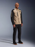 Alpinestars Dice Jacket, urban motorcykeljacka, Aluminum Black och khaki, tvåtonad design med svarta ärmar och khakifärgad torso, bärs av en modell med svarta byxor och svarta sneakers, arbetsklädesinspirerad estetik med praktiska fickor och broderad logotyp på ärmen.