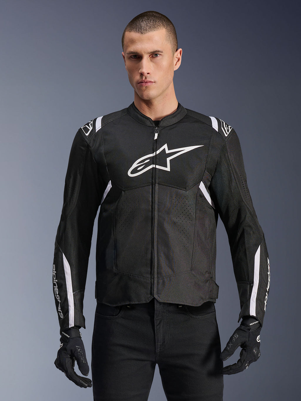 Alpinestars T-SPS Air V2 jacka, textil motorcykeljacka, svart med vita detaljer, stor vit bröstlogotyp, perforerad mesh-design för ventilation, bärs med svarta byxor och handskar