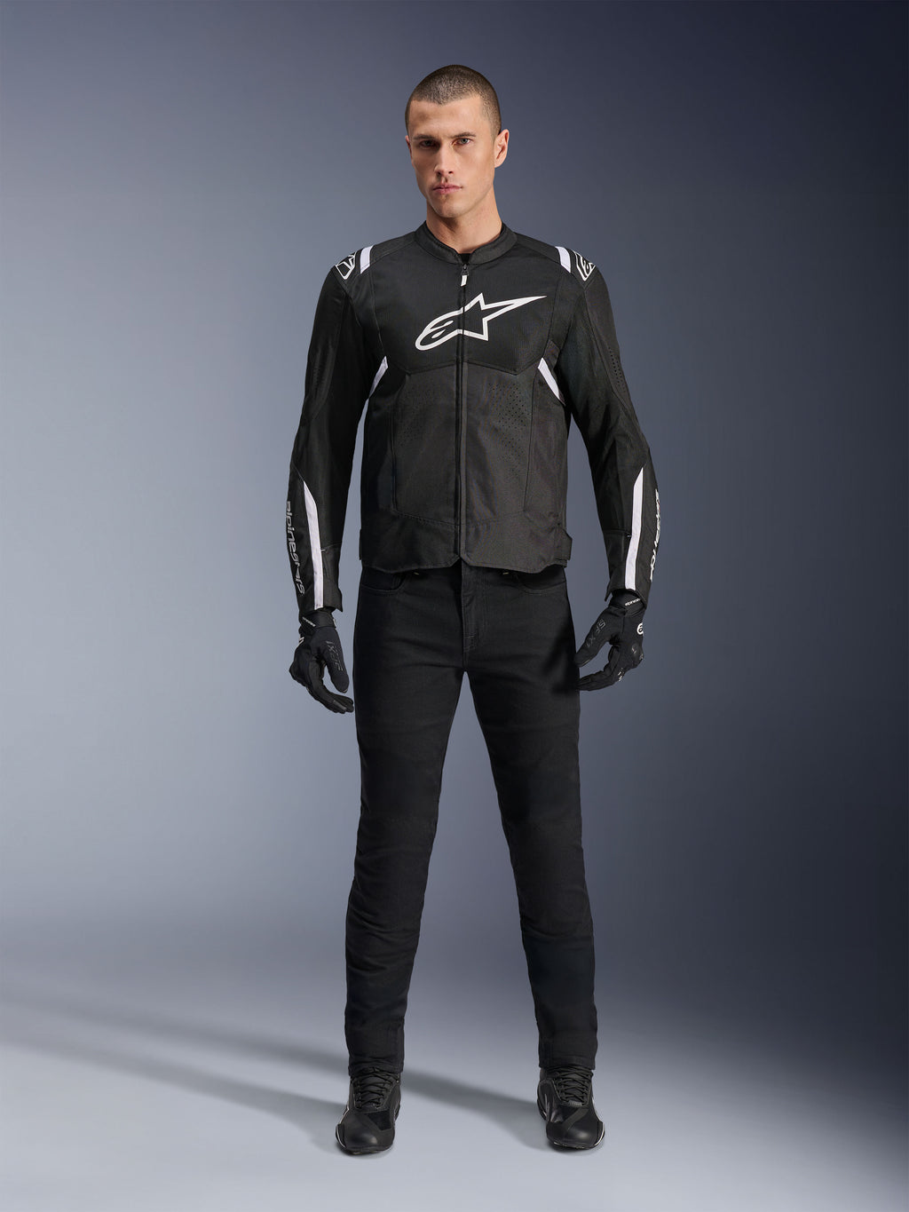 Alpinestars T-Sps Air V2 Jacket, svart och vit motorcykeljacka i textil, med en stor vit logotyp på bröstet och meshpaneler, bärs av en modell med svart utrustning för sportig stadskörning
