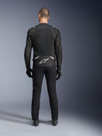 Alpinestars T-Sps Air V2-jacka, sedd bakifrån, svart och vit motorcykeljacka i textil, med en stor meshpanel på ryggen för maximalt luftflöde och vit Astars-logotyp på nedre ryggen, bärs med svarta mc-byxor och handskar