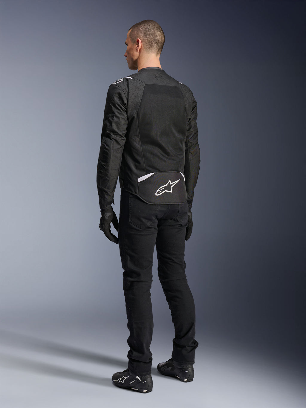 Alpinestars T-Sps Air V2-jacka, textil motorcykeljacka, svart, baksida som visar stor ventilationspanel i mesh och vit Alpinestars-logotyp på nedre delen av ryggen, kombinerad med svarta mc-byxor och handskar för en sportig urban stil.