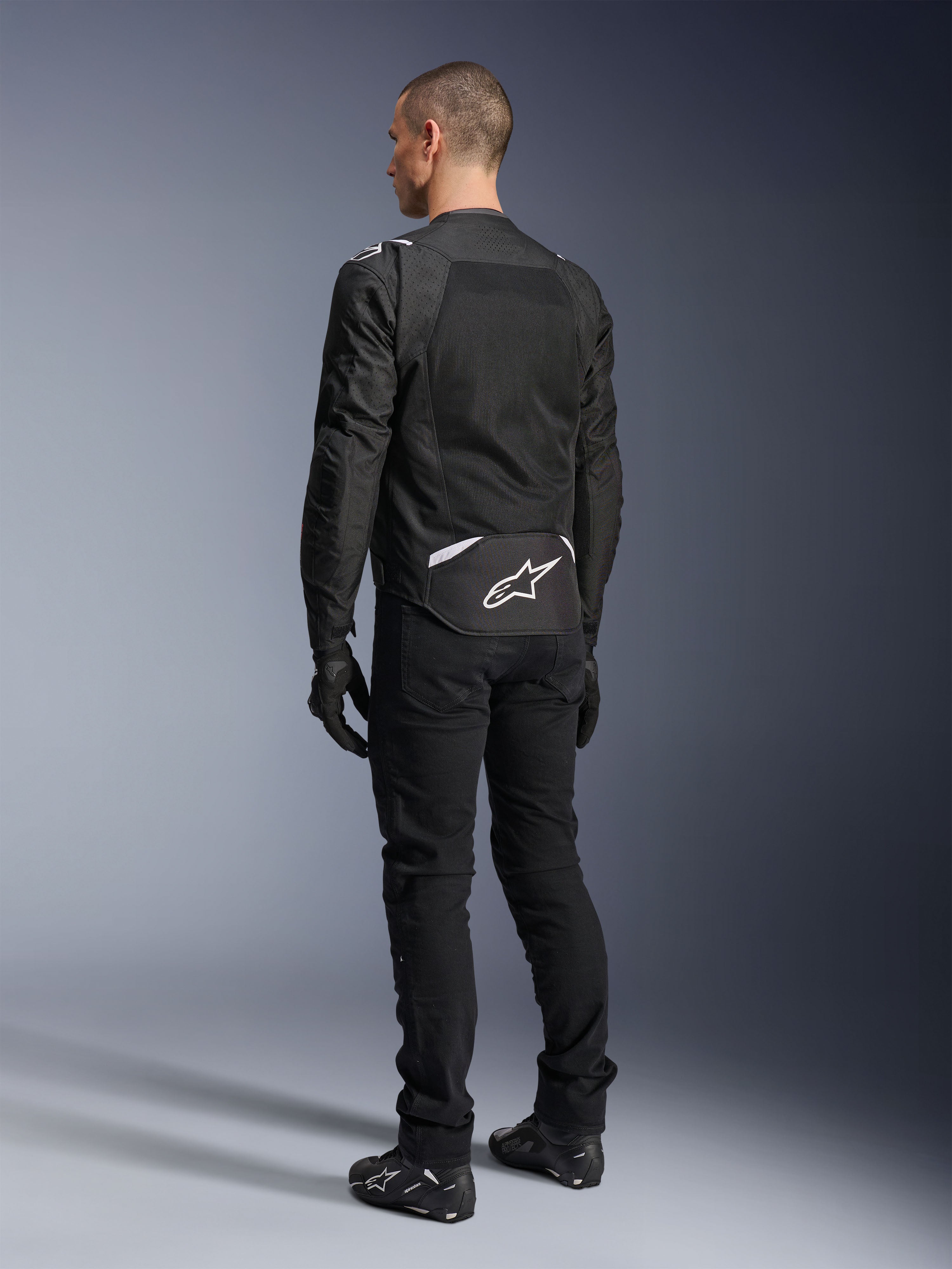Alpinestars T-Sps Air V2-jacka, textil motorcykeljacka, svart, baksida som visar stor ventilationspanel i mesh och vit Alpinestars-logotyp på nedre delen av ryggen, kombinerad med svarta mc-byxor och handskar för en sportig urban stil.