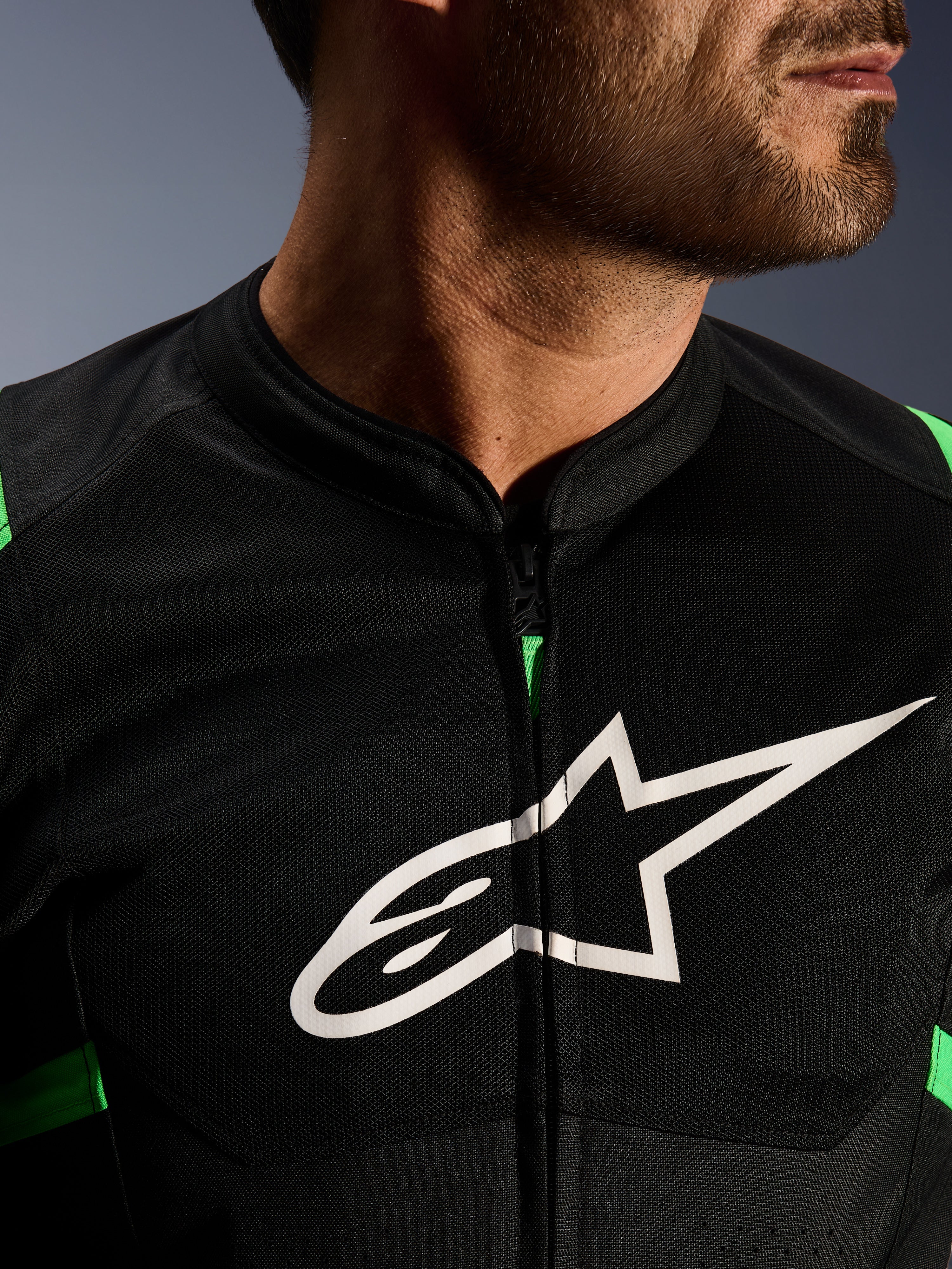 Close-up of Alpinestars T-SPS Air V2 Jacket, Black and Fluo Green, featuring breathable tech mesh panels, central zipper, and prominent white Alpinestars star logo on the chest, performance motorcycle gear