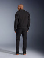 Alpinestars Bruiser Jacket in Black, back view of male model wearing the urban motorcycle jacket with matching black pants, featuring a small gold logo on the collar and adjustable waist straps, workwear-inspired aesthetic