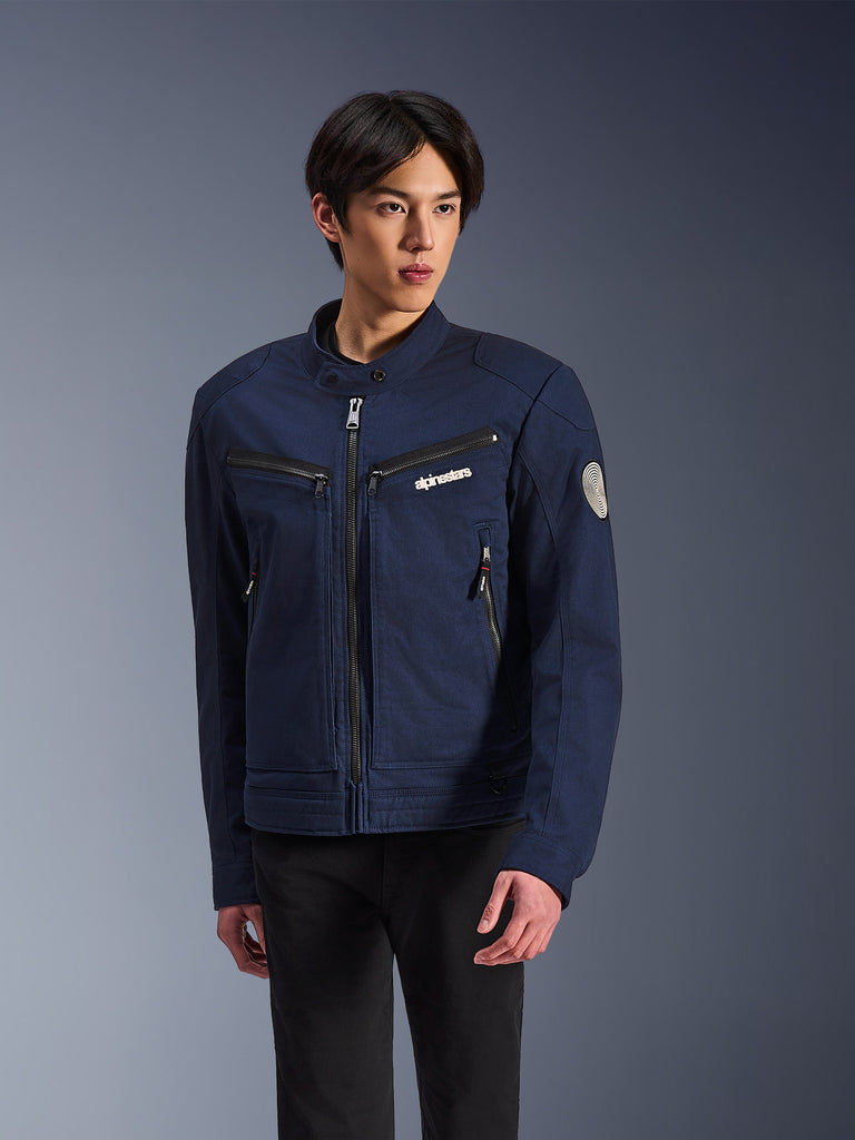 Alpinestars Bruiser Jacket, mörkblå motorcykeljacka med svarta dragkedjor, logotyp på bröstet och rund patch på ärmen, casual skyddsutrustning