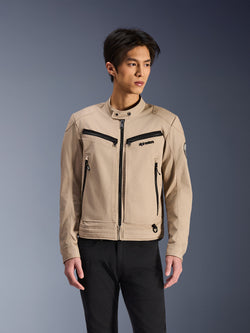 Alpinestars Bruiser-jacka, beige motorcykeljacka buren av manlig modell, med svarta dragkedjedetaljer på bröst och sidofickor, hög krage med tryckknapp, arbetsklädesinspirerad urban mc-stil, kombinerad med svarta byxor
