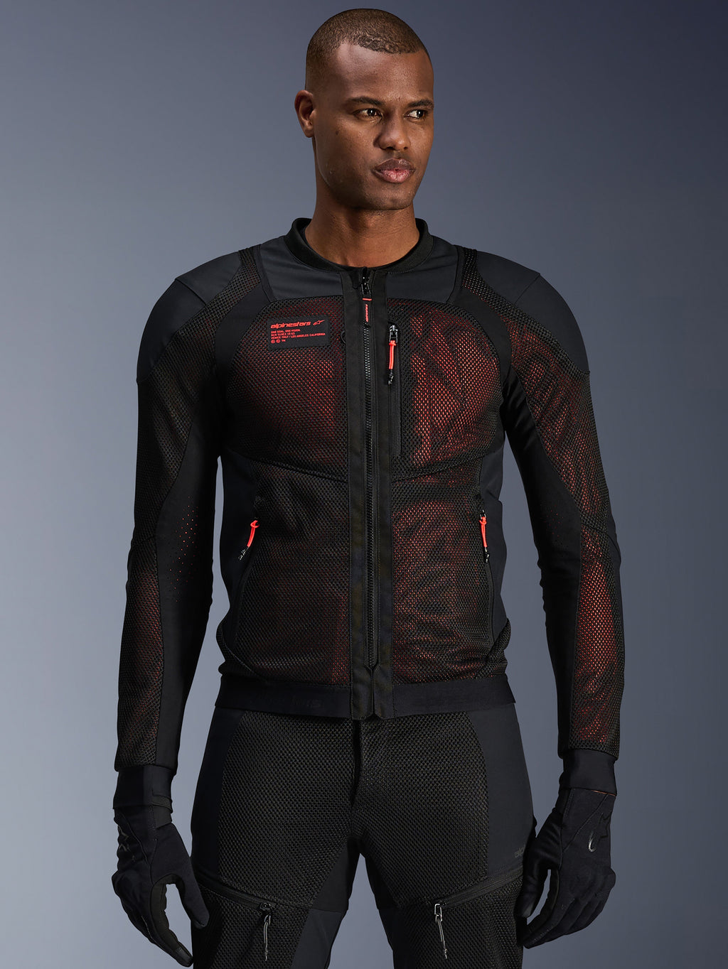 Alpinestars Troop-Air Pro Jacket, teknisk mesh-motorcykeljacka i svart och Red Fluo, bärs av en modell, med stora ventilationspaneler i mesh, rött underlager och röda dragtappar, urban körstil.