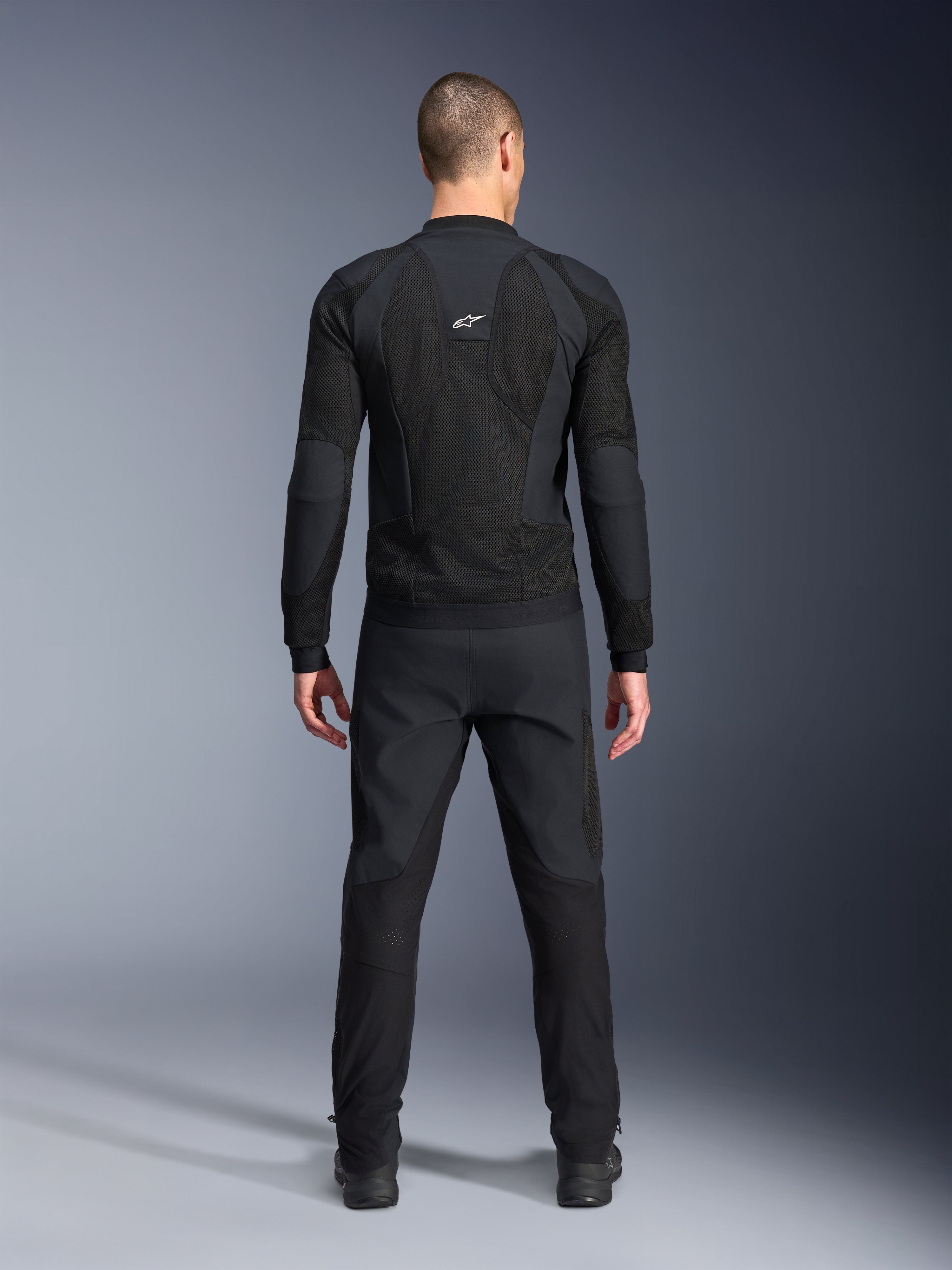 Alpinestars Troop-Air Pro jacka, sedd bakifrån, svart, teknisk motorcykeljacka med stora ventilationspaneler i mesh och vit Alpinestars-logotyp, kombinerad med svarta byxor, urban contemporary-körutrustning