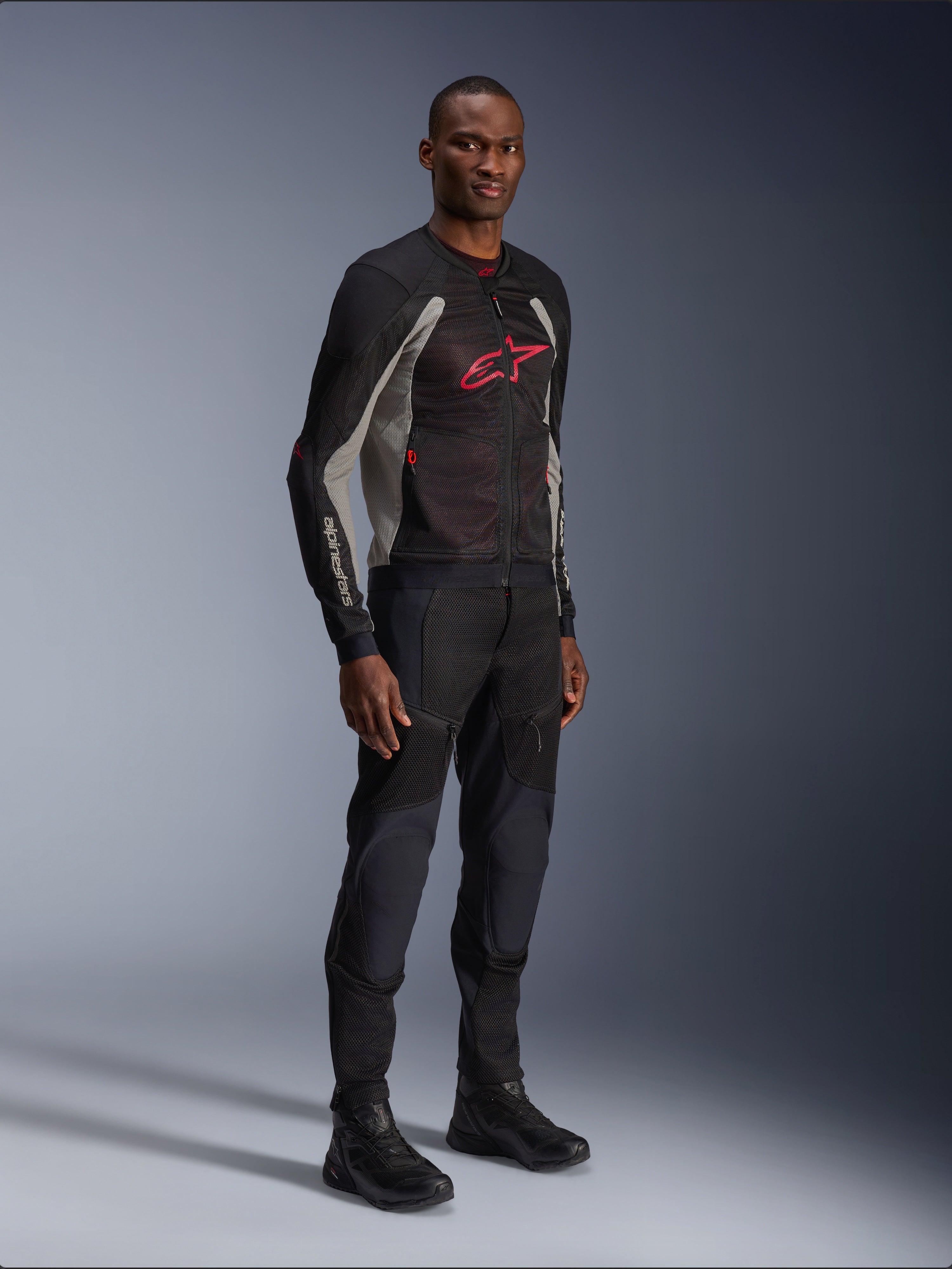 Alpinestars Troop-Air Jacket, technical mesh motorcycle jacket in Black, Ash Gray and Bright Red, worn by a model with matching black pants and boots, featuring a red Alpinestars logo on the chest, urban contemporary riding gear.