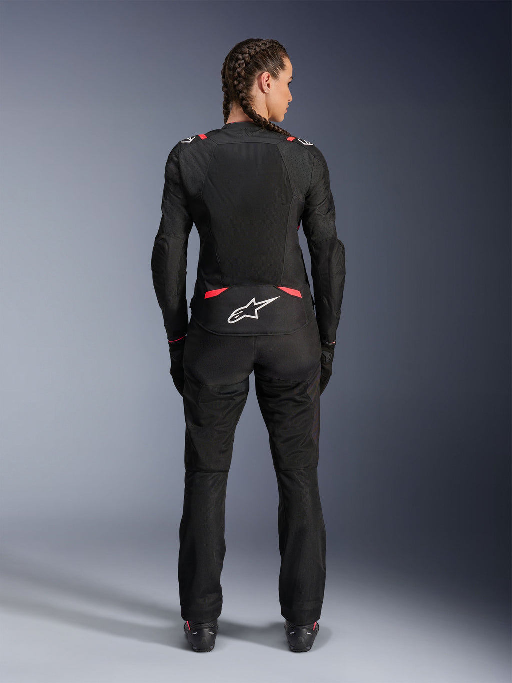 Alpinestars Stella T-SPS Air V2-jacka, motorcykeljacka i textil för dam, svart och Diva Pink, vy bakifrån på modell med flätat hår, med stora meshpaneler för ventilation, vit Astars-logotyp på nedre ryggen, matchad med svarta mc-byxor
