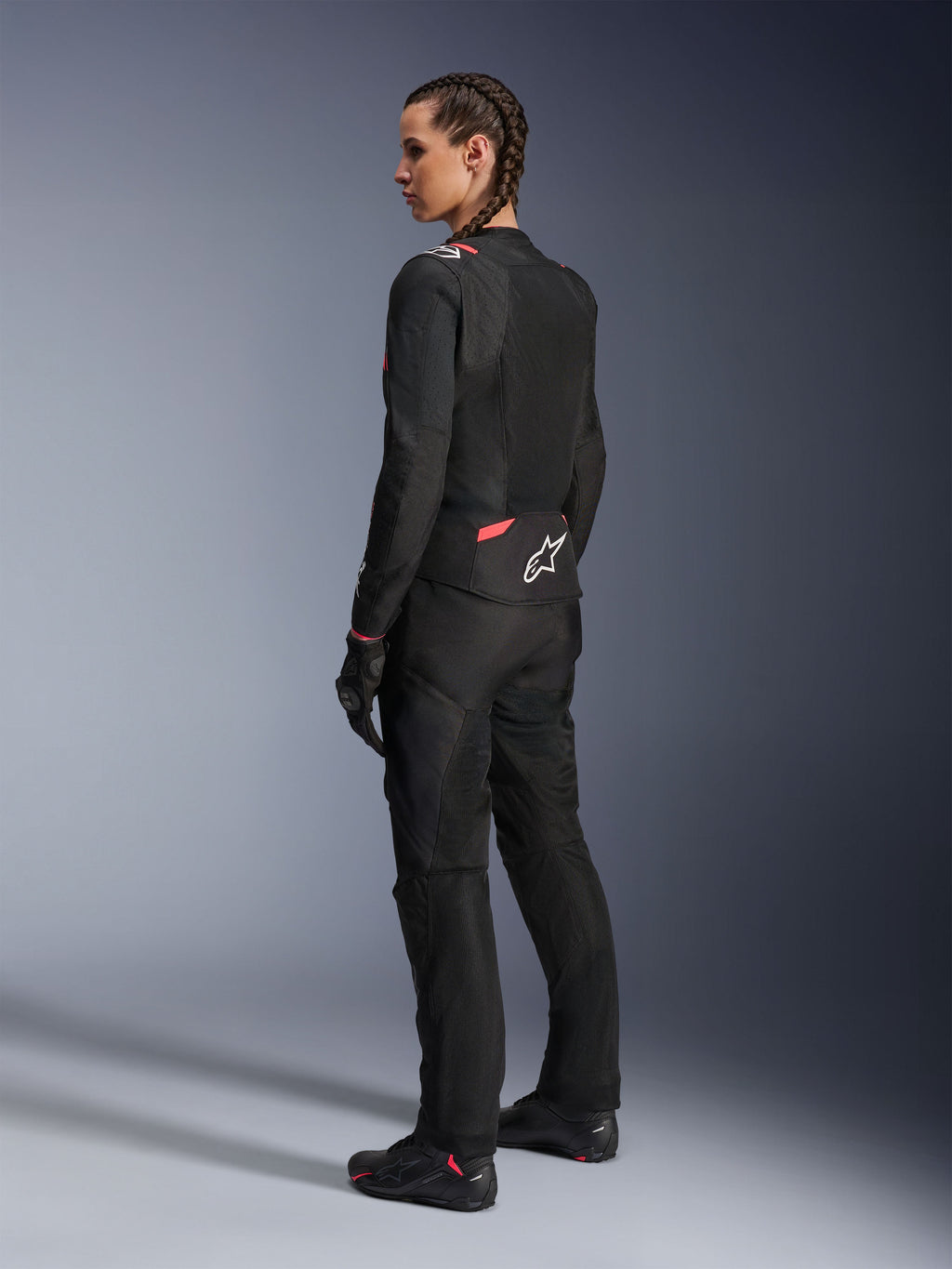 Alpinestars Stella T-Sps Air v2 damjacka, svart och Diva Pink, textilmotorcykeljacka sedd snett bakifrån, med stora meshpaneler för luftflöde och vit stjärnlogotyp på ryggen, bärs med matchande svarta mc-byxor, handskar och stövlar.
