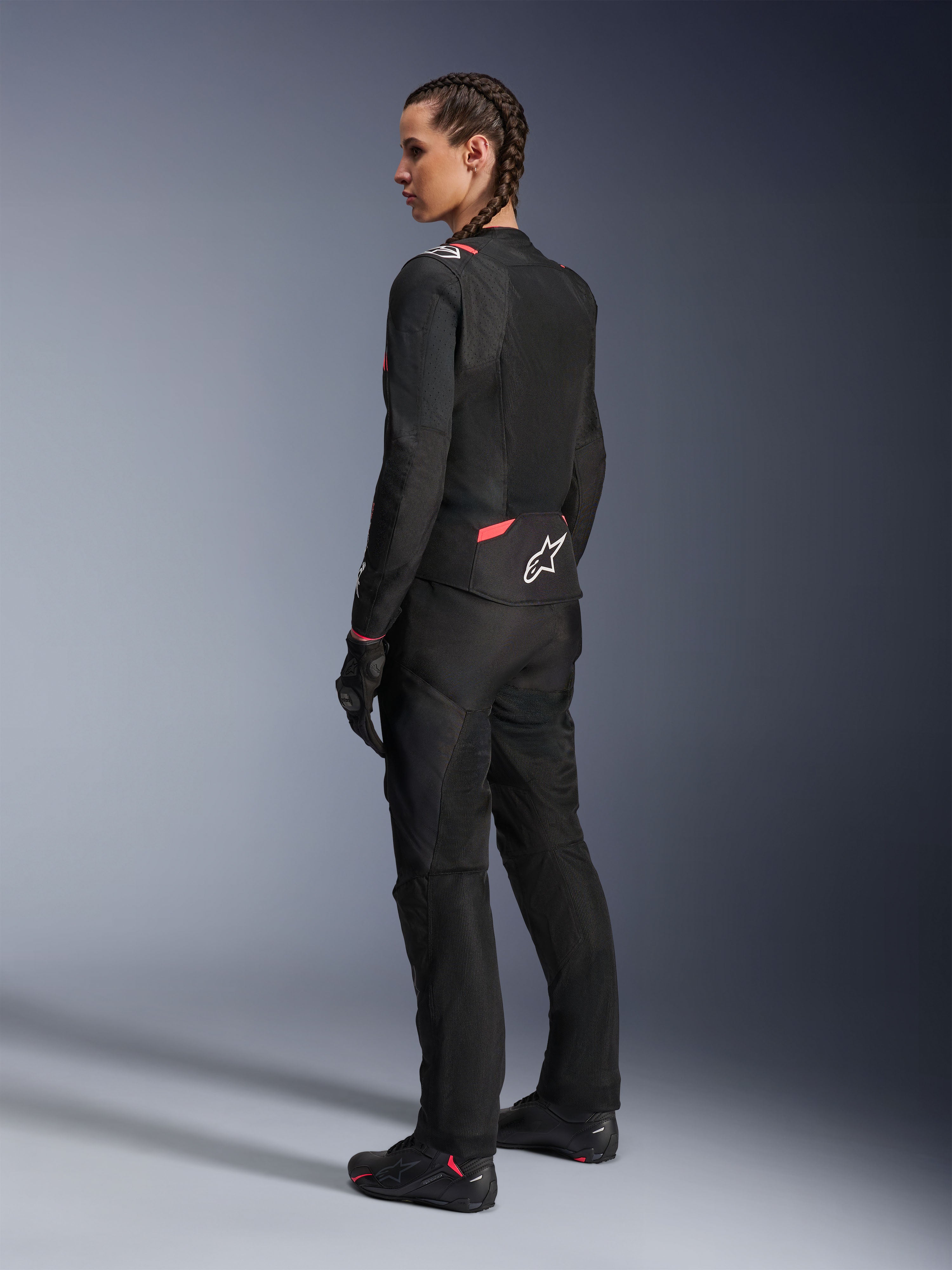 Alpinestars Stella T-Sps Air v2 damjacka, svart och Diva Pink, textilmotorcykeljacka sedd snett bakifrån, med stora meshpaneler för luftflöde och vit stjärnlogotyp på ryggen, bärs med matchande svarta mc-byxor, handskar och stövlar.