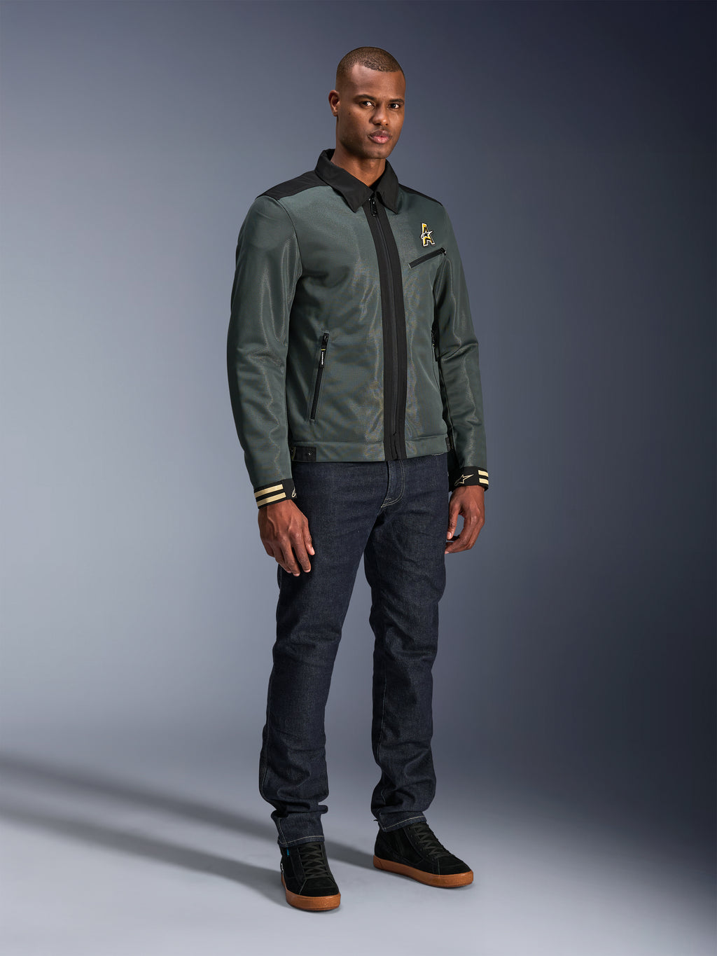Alpinestars Ignite Air Jacket, Urban Gray Black Blue, urban motorcycle jacket, worn by a model with dark denim jeans and black sneakers, featuring a mesh body, traditional shirt collar, Harrington-inspired silhouette, and gold Alpinestars branding.