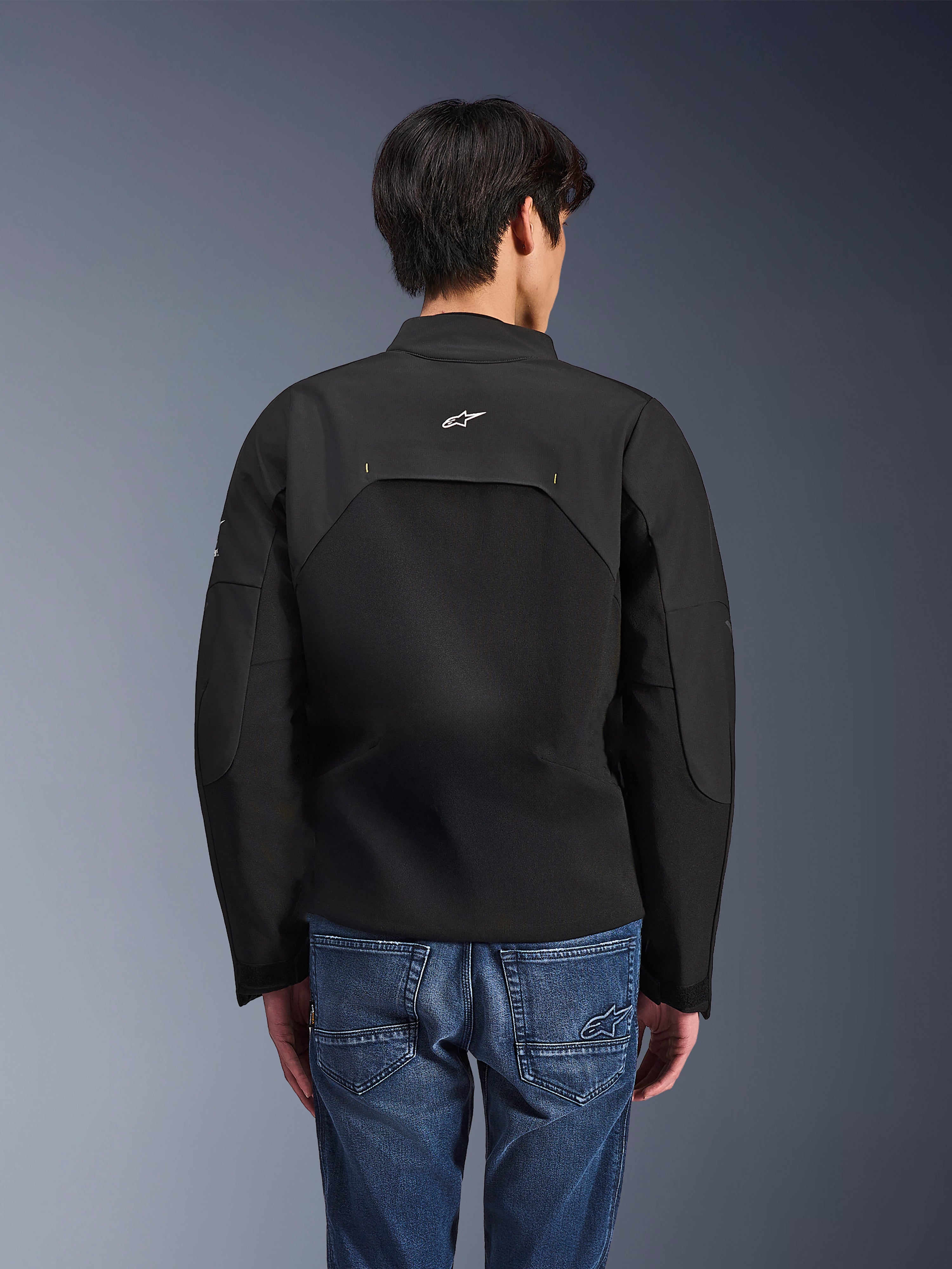 Alpinestars Provoke Jacket, Urban Motorcycle Jacket, Black, rear view showing white Astars logo and technical ripstop panels, worn with blue denim jeans, contemporary design for city commuting