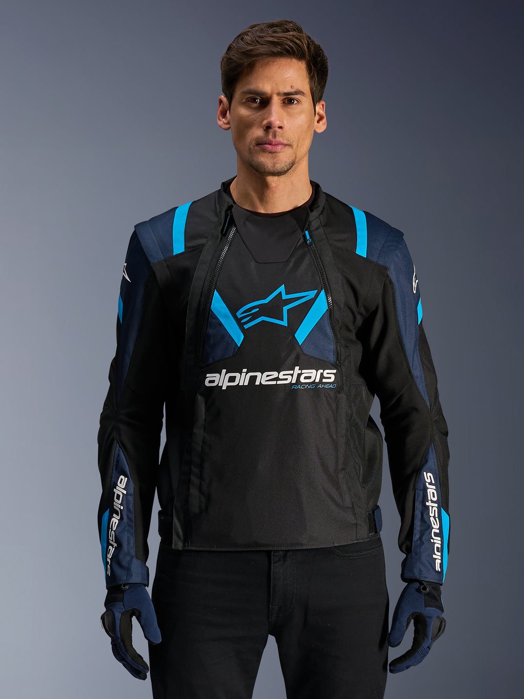 Alpinestars T-Stunt Air-jacka, motorcykeljacka i mesh, svart och blå, bärs av en modell med svarta byxor och handskar, med en modulär 2-i-1-design med ventilerande tech-mesh-paneler, stjärnlogotyp på bröstet och Alpinestars-logotyp på ärmarna.