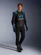 Manlig modell i Alpinestars T-Stunt Air-jacka, svart, mörkblå och Blithe Blue, med framträdande meshpaneler för luftflöde, matchad med svarta byxor och körhandskar, sportig motorcykeljacka för sommarkörning på väg.