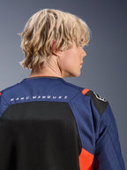Alpinestars MM93 T-SPS Air V2-jacka, mörkblå och svart med röda fluo-detaljer, närbild på övre ryggen med 'MARC MARQUEZ'-logotyp, ventilerande meshpaneler och perforerad textilkonstruktion, bärs av en blond modell.
