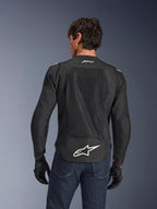 Alpinestars FQ20 T-SPS Air V2 Monster-jacka, svart, vy bakifrån med stora ventilationspaneler i mesh och vit Alpinestars-logotyp på nedre delen av ryggen, bärs med blå jeans och svarta motorcykelhandskar, urban sportig körstil.