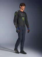 Manlig förare som bär Alpinestars FQ20 T-SPS Air V2 Monster-jacka i svart, med '20'-logotypen och Monster Energy-klon på bröstet, kombinerat med mörka MC-jeans, svarta MC-skor och matchande FQ20-handskar, studiobild i helfigur.