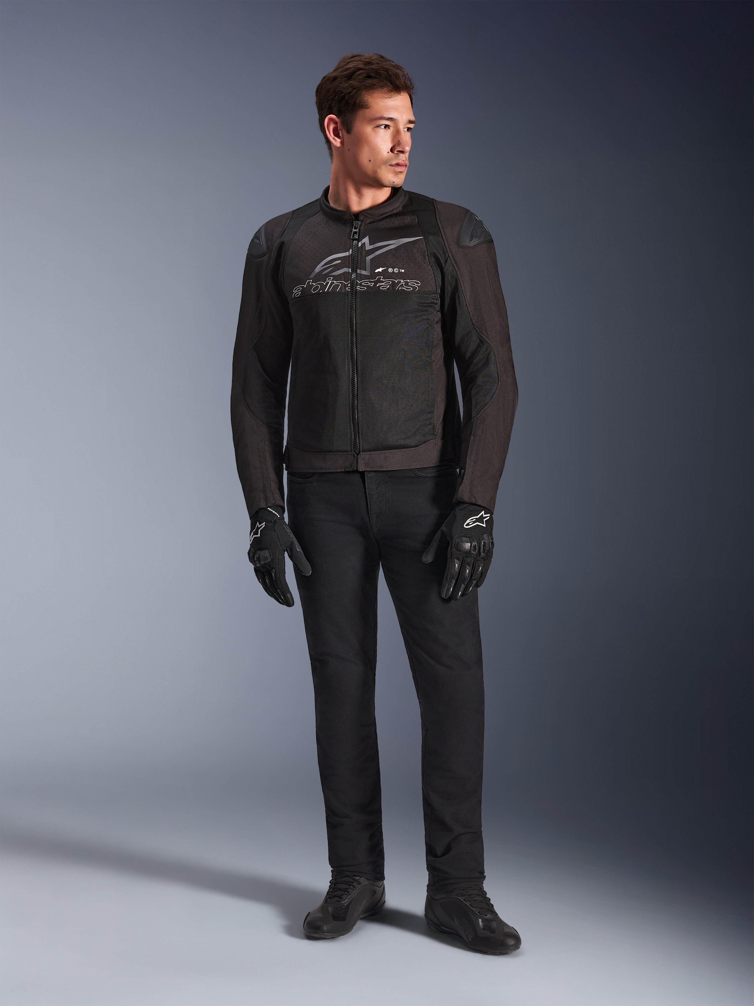 Manlig modell som bär Alpinestars SMX Air Jacket, motorcykeljacka i färgen Black Anthracite med ventilerade meshpaneler och grå logotyp på bröstet, matchad med svarta byxor och skyddshandskar, studiomiljö med tonad bakgrund