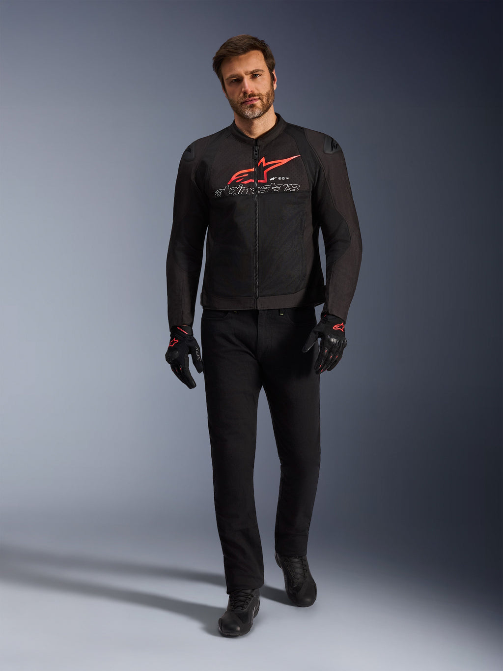 Alpinestars SMX Air Jacka, svart, klar röd och vit, sportig motorcykeljacka buren med svarta körbyxor och handskar, med tekniska meshpaneler och en framträdande röd Alpinestars-logotyp på bröstet, outfit för högpresterande gatkörning