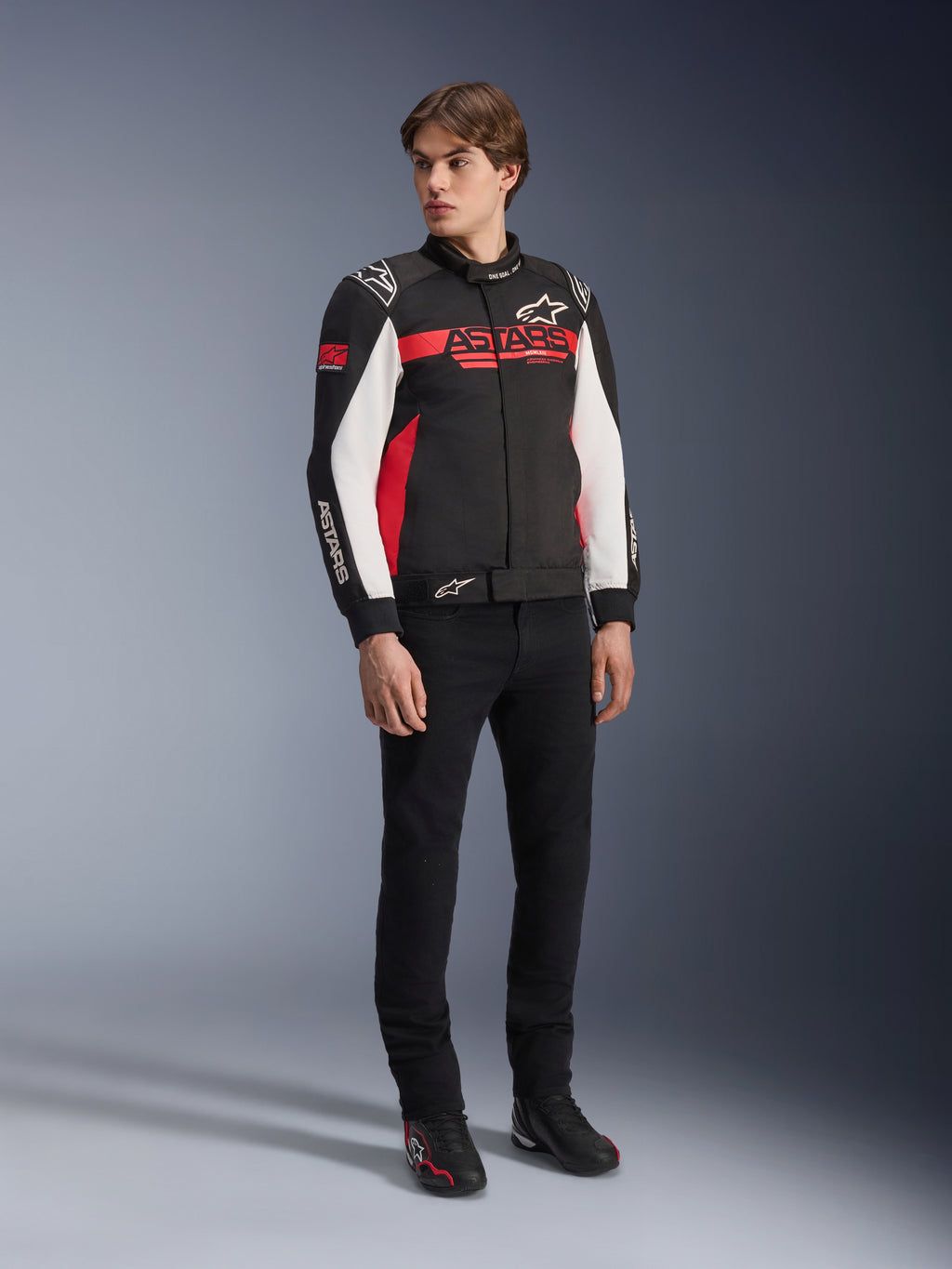 Alpinestars Monza Sport-jacka, svart, klarröd och vit, motorcykeljacka i textil, racinginspirerad design med ASTARS-logotyper på bröstet och ärmarna, bärs av en modell med svarta byxor och körskor, avslappnad sportig körutrustning