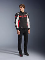Alpinestars Monza Sport-jacka, svart, klarröd och vit, motorcykeljacka i textil, racinginspirerad design med ASTARS-logotyper på bröstet och ärmarna, bärs av en modell med svarta byxor och körskor, avslappnad sportig körutrustning