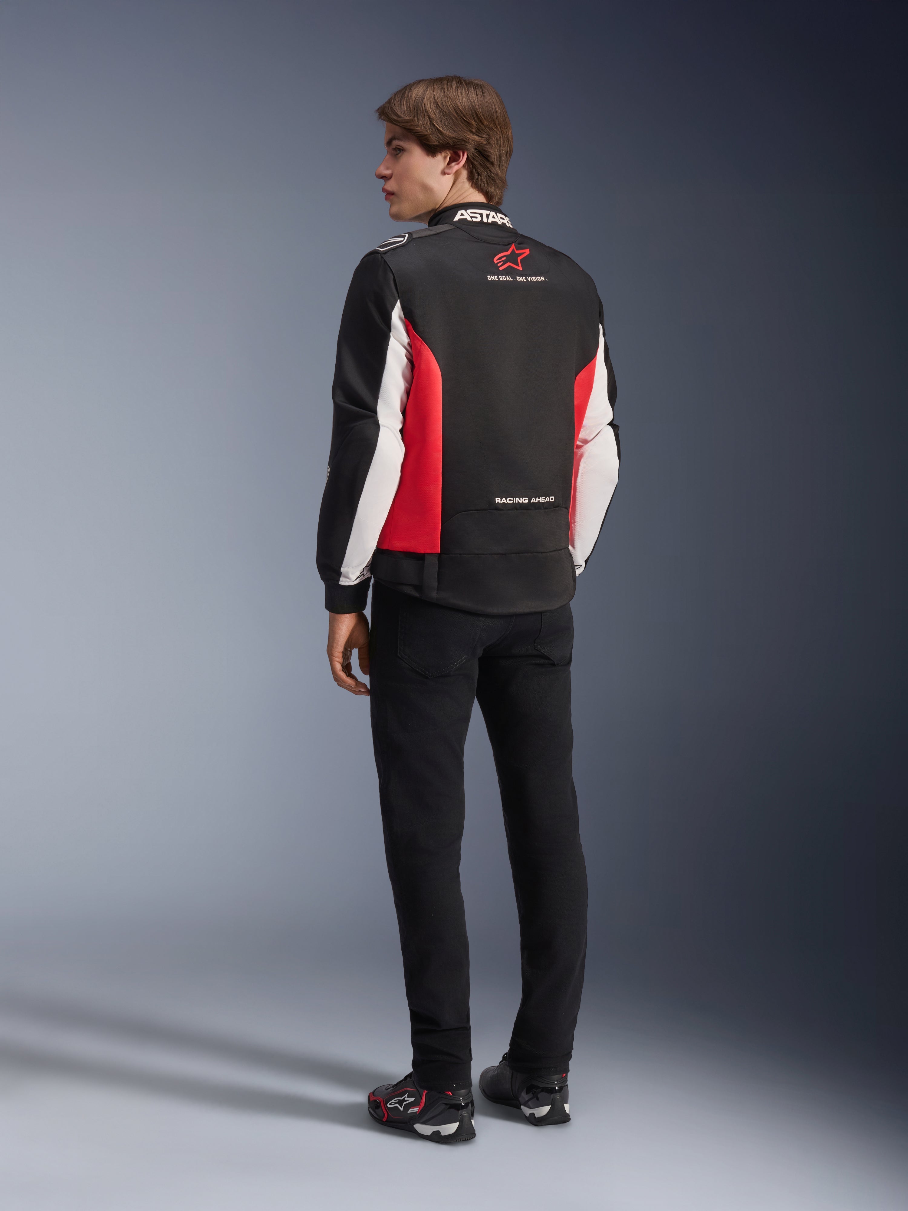 Alpinestars Monza Sport-jacka, textiljacka för motorcykel, svart, klarröd och vit, ryggvy av modell med röda sidopaneler och vita ärmdetaljer, Alpinestars-logotyp och texten 'ONE GOAL. ONE VISION.', kombinerad med svarta byxor och körskor för en sportinspirerad look