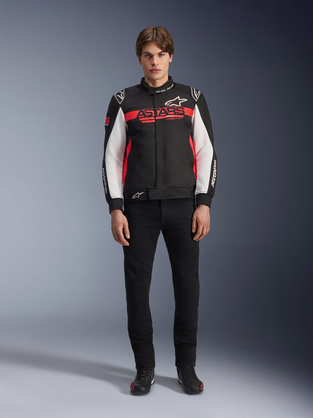 Manlig modell iklädd Alpinestars Monza Sport Jacket i svart, klarröd och vit, med en stor röd ”ASTARS”-logotyp över bröstet och vita paneler på ärmarna, kombinerad med svarta byxor och svarta mc-stövlar.
