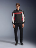 Manlig modell iklädd Alpinestars Monza Sport Jacket i svart, klarröd och vit, med en stor röd ”ASTARS”-logotyp över bröstet och vita paneler på ärmarna, kombinerad med svarta byxor och svarta mc-stövlar.