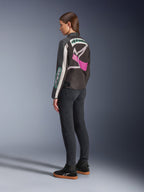 Alpinestars Idles damjacka, motorcykeljacka, svart, off-white och lila, sedd bakifrån på modell, med en stor omslutande Alpinestars-logotyp och vintage racing-inspirerad design, matchad med mörka jeans och svarta skor