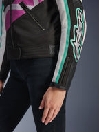 Alpinestars Idles damjacka, närbild av ärmen och sidan av överkroppen, svart med lila, vita och turkosa detaljer, med en framträdande Alpinestars-logotyp på armen, manschett med dragkedja och tryckknapp samt justeringsrem i midjan, vintageinspirerad motorcykelutrustning.