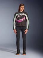 Kvinna i Alpinestars Idles damjacka, svart, benvit och lila, vintage racing-inspirerad design med stor omslutande logotyp och blågröna detaljer, stylad med svarta jeans och mc-sneakers, urban motorcykelutrustning