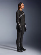 Kvinna i Alpinestars Stella T-SPS Air V2-jacka, svart och vit, stylad med svarta motorcykelbyxor, handskar och stövlar, med vit Alpinestars-logotyp på bröstet och ärmen, helfigur i trekvartsvy från sidan
