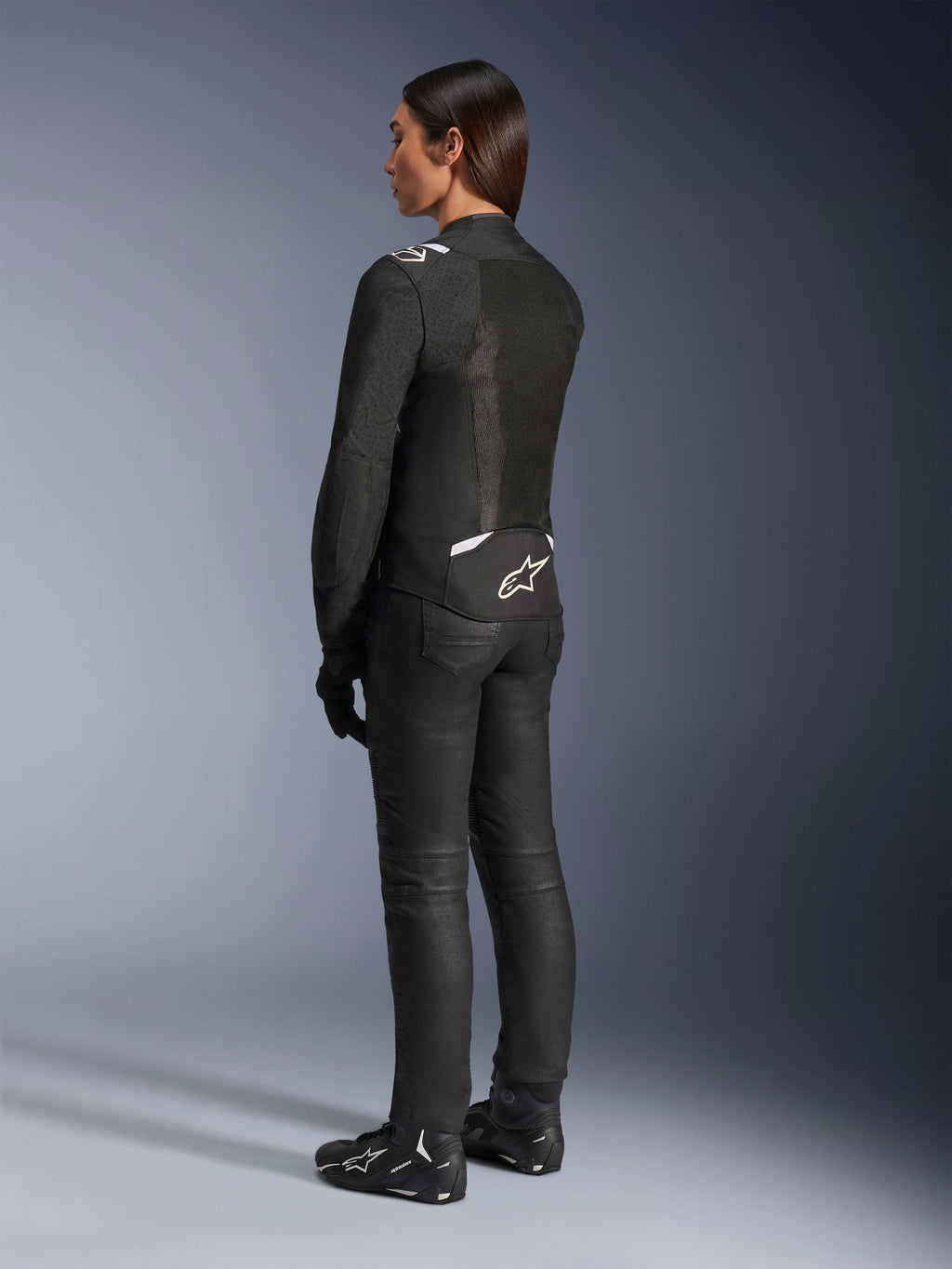 Alpinestars Stella T-Sps Air V2-jacka, svart och vit, vy bakifrån som visar meshpaneler och logotyp på nedre ryggen, matchad med svarta mc-byxor och motorcykelskor, sportig textilutrustning för kvinnor