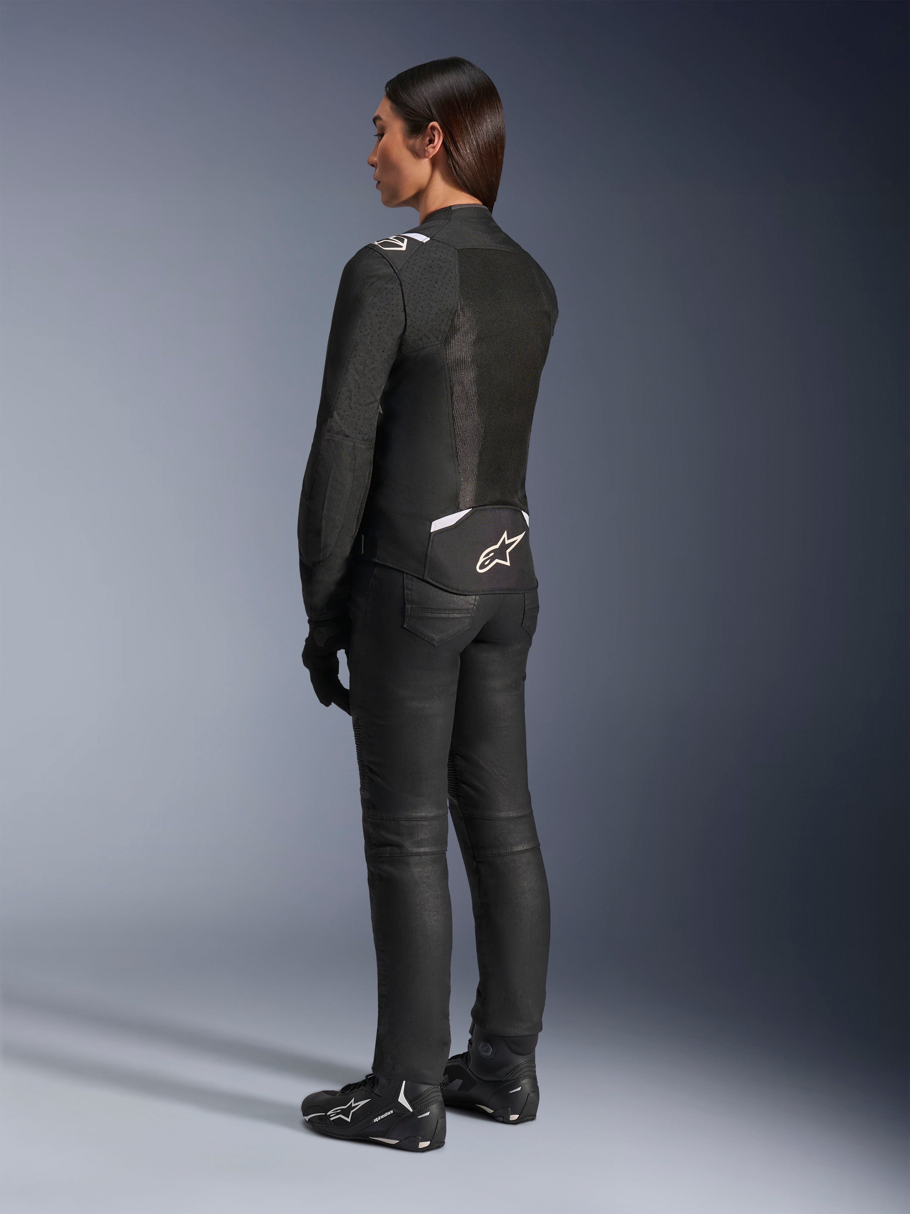 Alpinestars Stella T-Sps Air V2-jacka, svart och vit, vy bakifrån som visar meshpaneler och logotyp på nedre ryggen, matchad med svarta mc-byxor och motorcykelskor, sportig textilutrustning för kvinnor