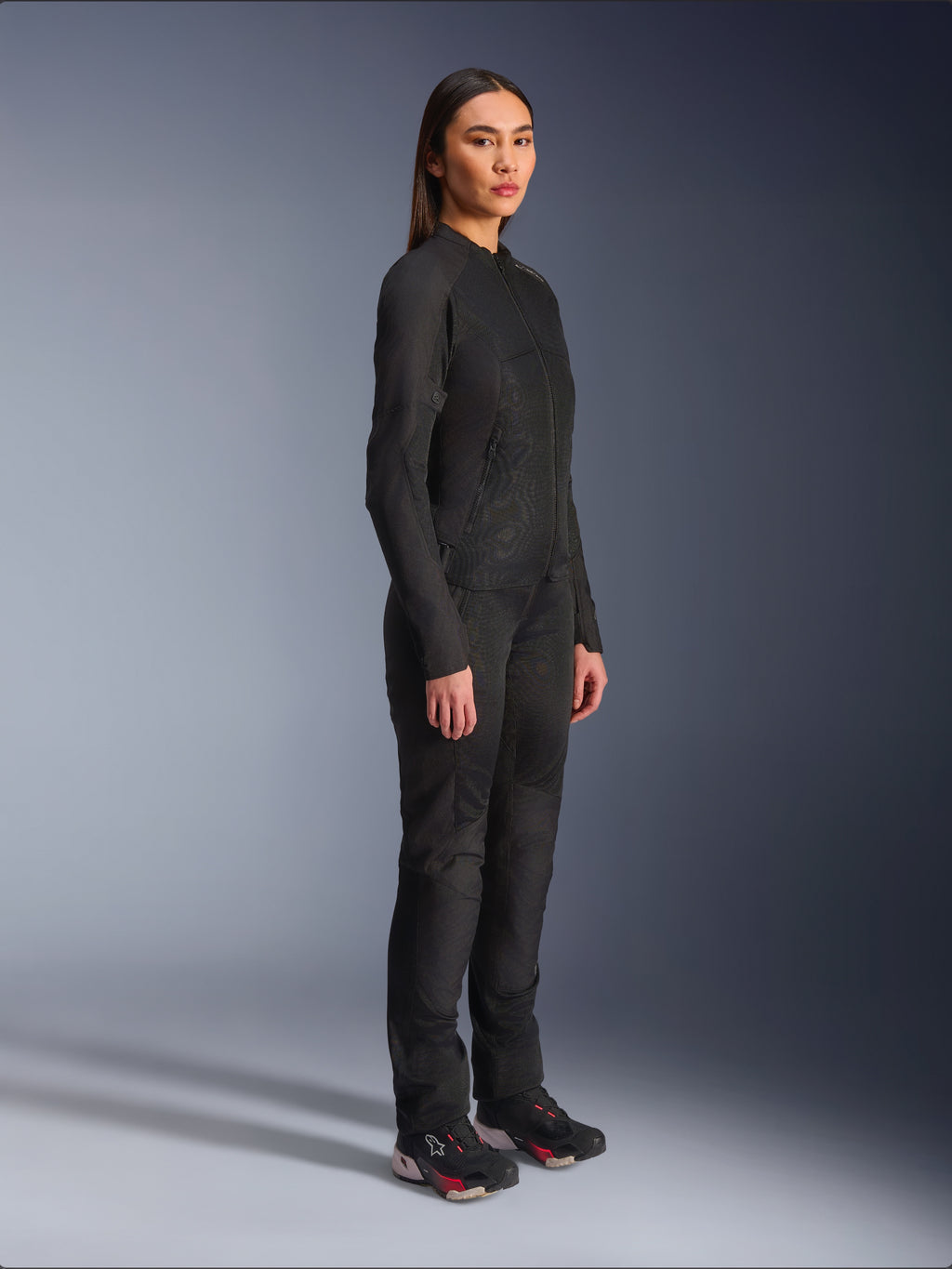 Alpinestars Woman Stella C-1 Air Jacket in Black, textile motorcycle jacket with mesh panels, worn with matching black riding pants and technical sneakers, studio shot showing a full-length urban riding outfit.