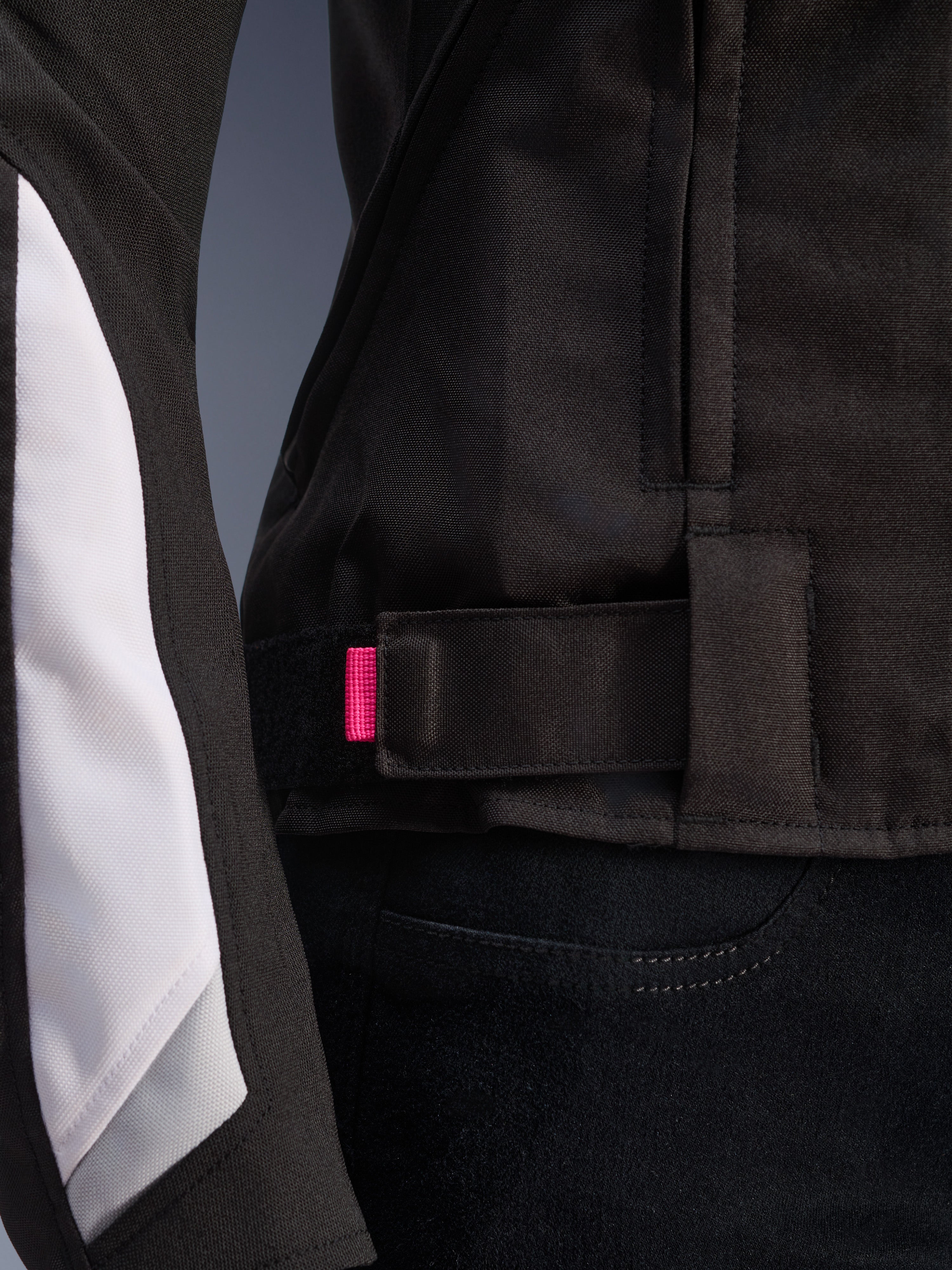 Alpinestars Stella T-GP Plus R V4 Jacket, Black and White, close-up of the adjustable waist strap with pink accent tab, durable textile construction with white sleeve paneling, sport-fit women's motorcycle jacket.