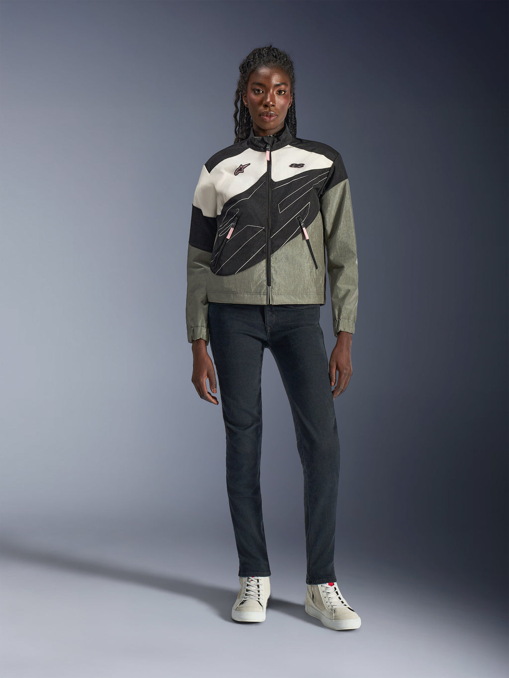 Alpinestars Stella Moshell-jacka, motorcykeljacka för dam, svart, grå och off-white med rosa detaljer, bärs av en modell med mörka jeans och off-white sneakers, med asymmetrisk dragkedja och djärv geometrisk grafik, modern urban mc-utrustning