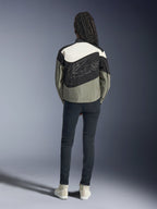Ryggvy av en modell som bär Alpinestars Stella Moshell-jackan i svart, grått och off-white, med en asymmetrisk design och en stor stiliserad konturlogotyp på ryggen, kombinerat med mörka slim-fit jeans och vita sneakers, urbana streetwear-inspirerade motorcykelkläder för kvinnor.