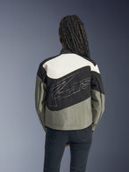 Kvinna sedd bakifrån i Alpinestars Stella Moshell-jacka, svart, grå och off-white urban motorcykeljacka med en stor vit konturerad logotyp på ryggen, matchad med svarta byxor, modern streetwear-inspirerad mc-utrustning.