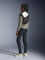 Kvinna som bär Alpinestars Stella Moshell-jacka, urban motorcykeljacka i färgerna svart, grått och off-white, baksida med asymmetrisk paneldesign och stor grafik på ryggen, stylad med svarta slim-fit-byxor och off-white sneakers, modern urban motorcykelutrustning
