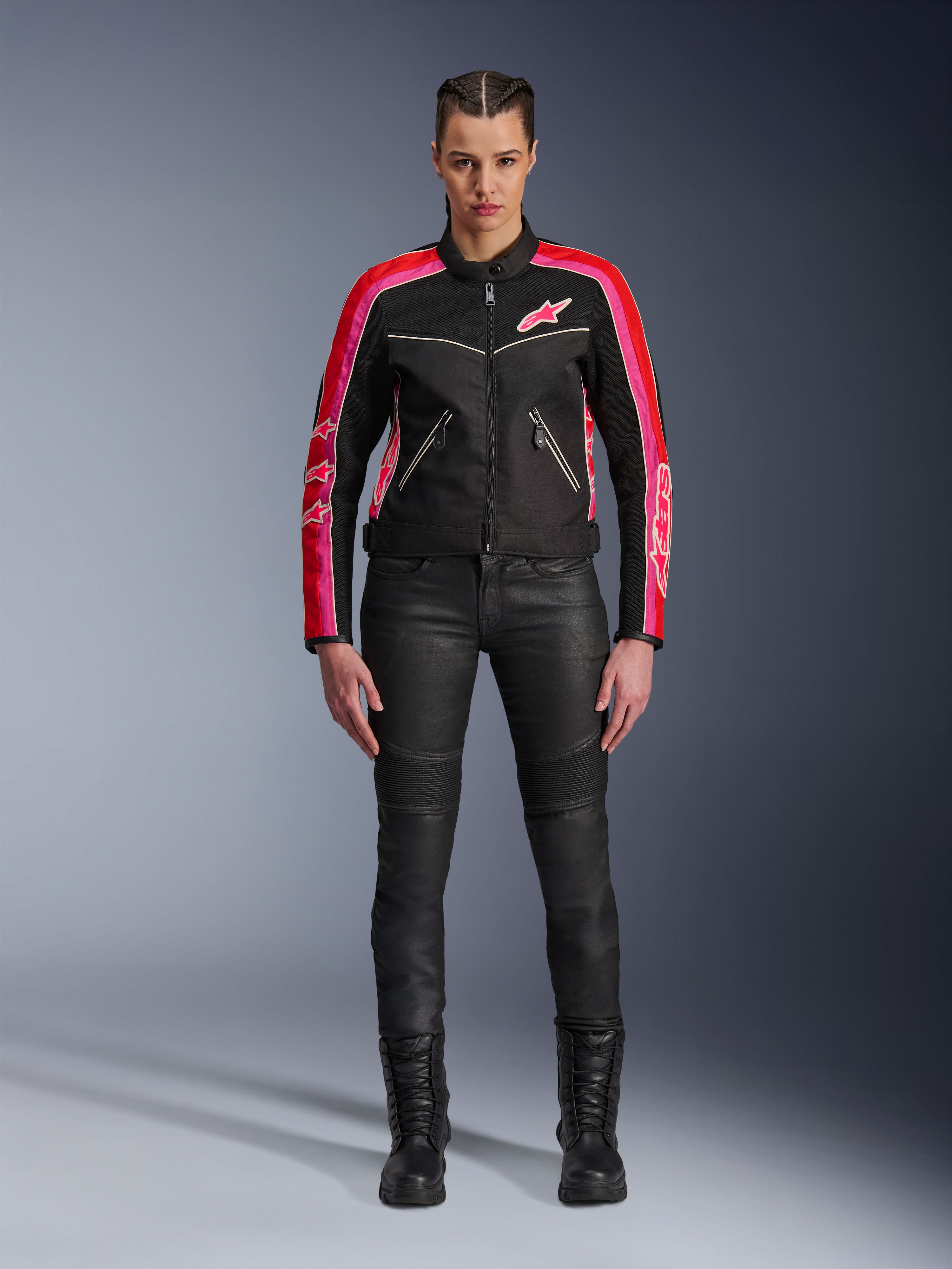 Female rider wearing the Alpinestars Stella T-Dyno Air Jacket, Black with Bright Red and Fuchsia accents, paired with black motorcycle pants and lace-up boots, featuring 3D mesh panels, tailored fit, and pink star logos, urban riding gear outfit