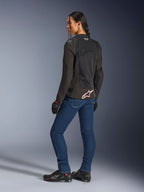 Alpinestars Stella SMX Air-jacka, svart med vit och röd logotyp, bärs av en kvinnlig förare sedd från en trekvartsvy bakifrån, stylad med blå motorcykeljeans och svarta körskor, med teknisk mesh-konstruktion för sportkörning i varmt väder.