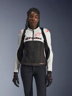 Alpinestars Stella SMX Air jacka för dam, isgrå, svart och Coral Fluo, med meshkonstruktion och perforerade paneler, bärs av en kvinnlig modell med svarta motorcykelhandskar och byxor, vy framifrån.
