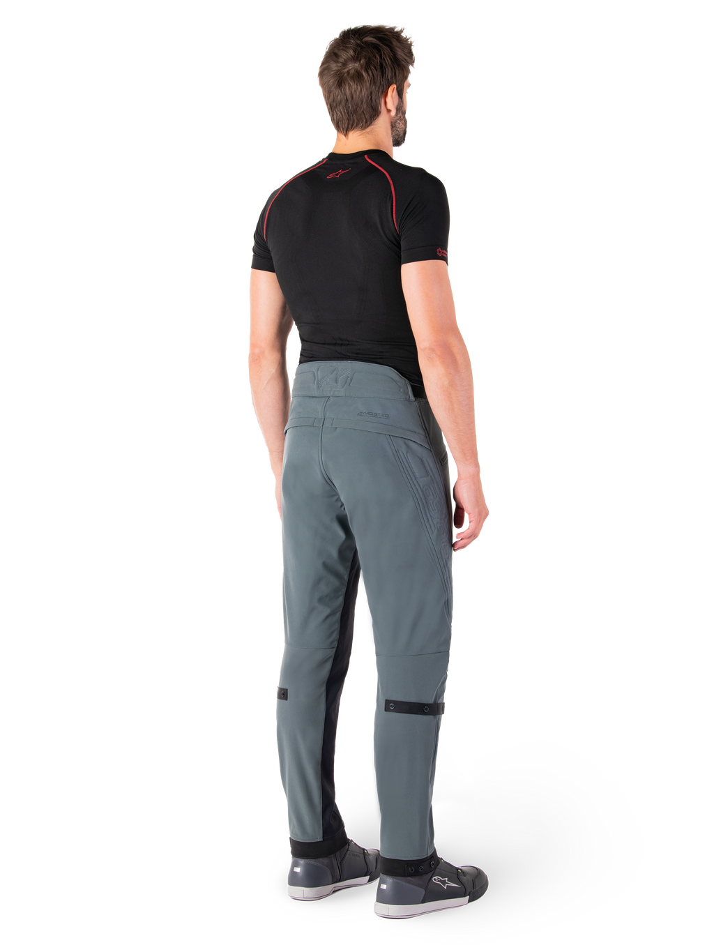 Alpinestars Alden byxor, Urban Gray, sedda bakifrån, tekniska motorcykelbyxor i textil med kviltade detaljer på den övre bakre linningen och benen, kombinerade med ett svart baslager och grå motorskor, modern urban streetwear-stil.